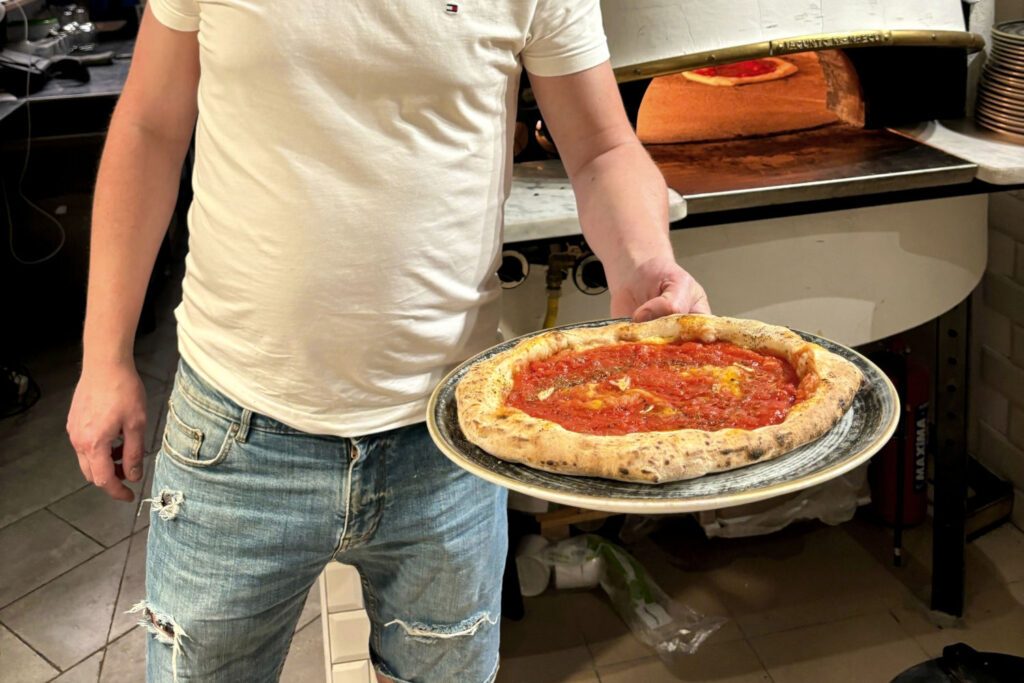Pizzaiolo kész nápolyi pizzával a kemence előtt