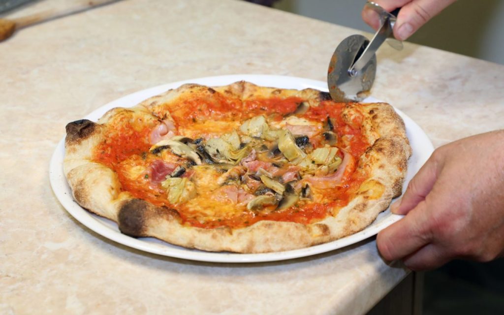 Frissen sült pizza szeletelése a Studio Italia élményfőzésén